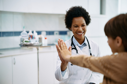 Happy African American pediatrician giving high five to a kid after medical examination at doctor's office.