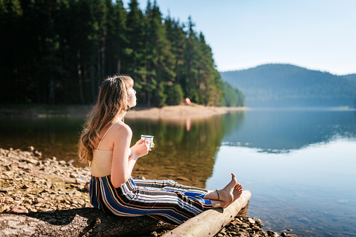 Cute female holding a mug in front of a mountain lake