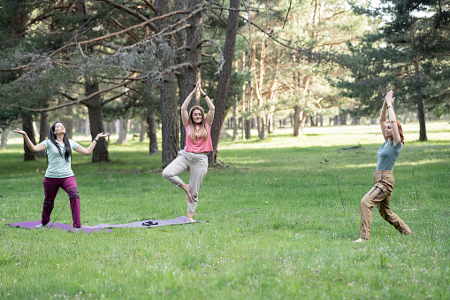 three mature women do yoga outdoors in nature, focus on blonde woman.
