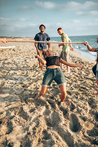 Multicultural friends having fun together with limbo game at the beach