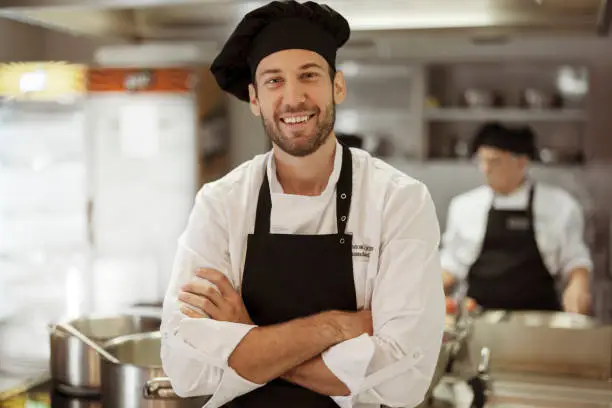 Portrait of satisfied cheerful positive chef in restaurant kitchen looking at camera