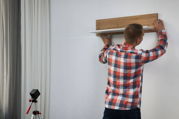 istock Man using cross line laser level for hanging wooden shelf on light wall indoors, back view 1422161747