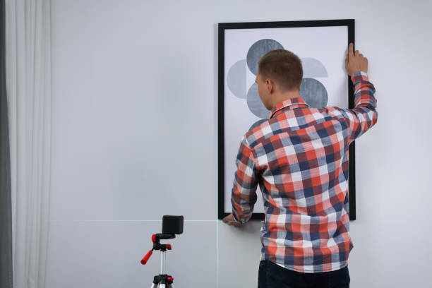 istock Man using cross line laser level for hanging painting on light wall, back view 1422161794
