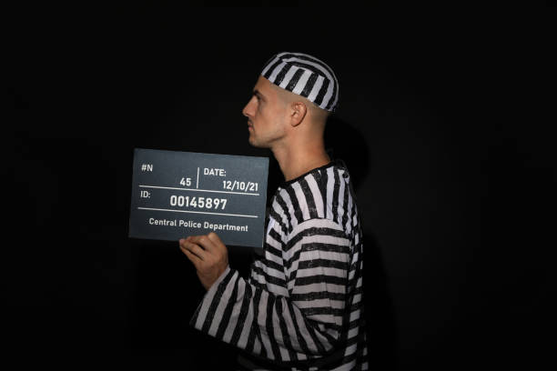 istock Mug shot of prisoner in striped uniform with board on black background, side view 1422162642