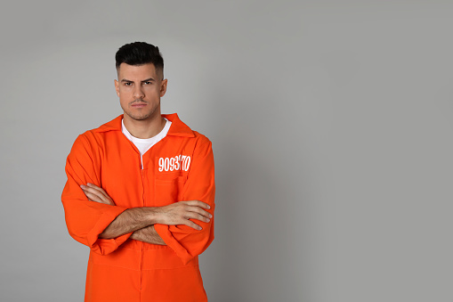 Prisoner in orange jumpsuit on grey background, space for text
