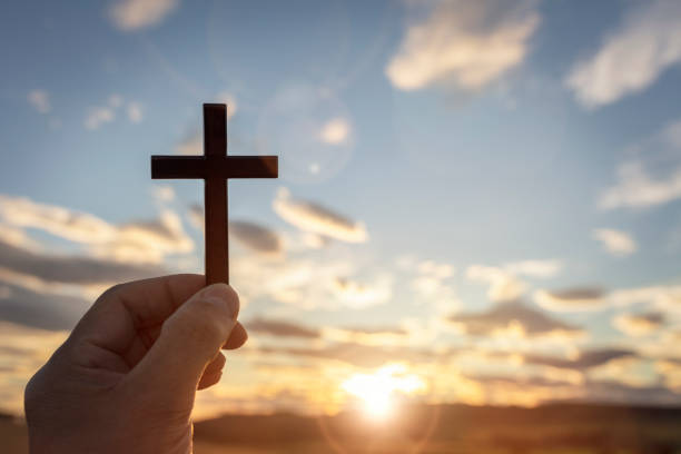 holding up religious cross crucifix to sky at sunset background - cross shape religion sky wood imagens e fotografias de stock