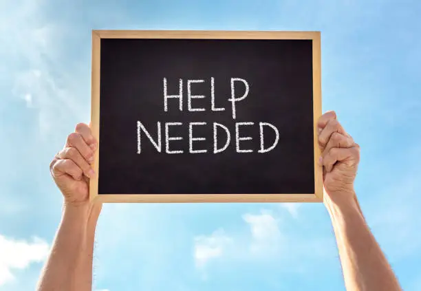 Photo of Help needed sign held up by man against blue sky background