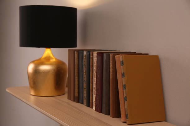 istock Wooden shelf with different books and lamp on light wall 1422165167