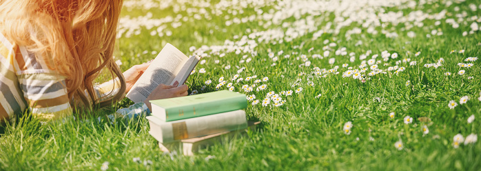 Young woman lying on the field and reading some books. Concept of hobby, relaxing and studying.