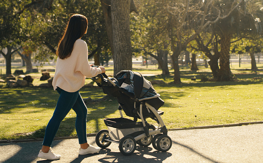 Fitness, mother and walking with baby stroller with a woman enjoying fresh air at a family park while pushing carriage. Adoption and motherhood while walking for fun, exercise and wellness in nature