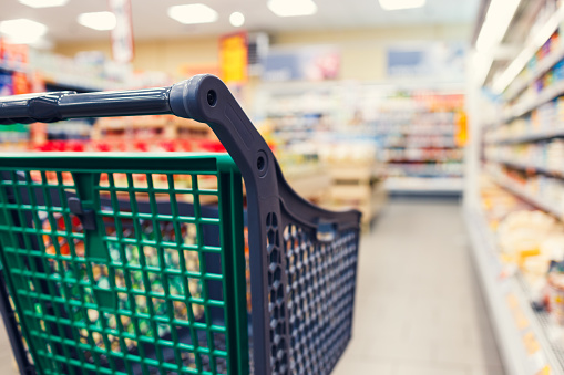 Empty grocery cart in the store. The shopping cart is in selective focus, the background of the store is blurred.