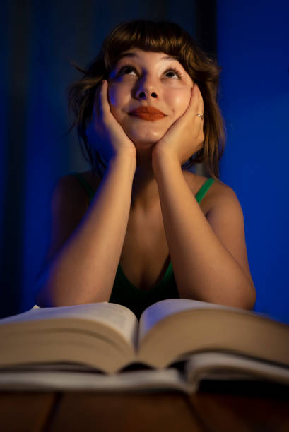 istock Young woman reading a book in dim light and contemplating 1422185614