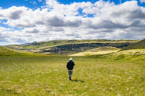 Teenage boy walking over grass meadow in the vicinity of the  Reykjadalur Hot Spring Thermal River, South Western Iceland.