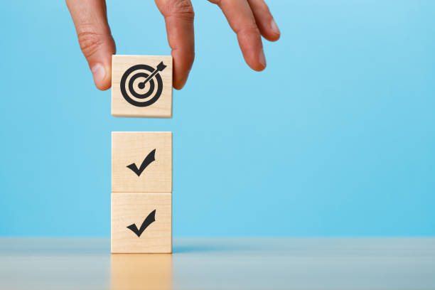 istock Hand putting stack of wooden blocks with marks and target icons on a blue background copy space. 1422187559