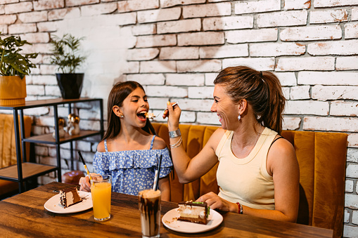 Beautiful young girl eating a slice of chocolate cake in a café with her mother.