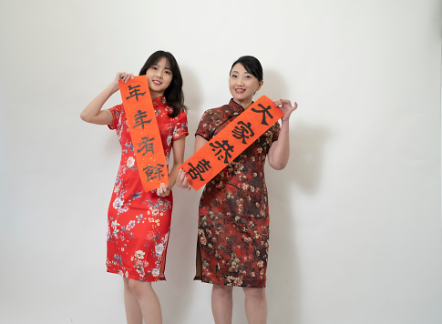 Happy asian young woman and mother showing Spring Festival couplets.Chinese characters mean:\nCongratulations everyone,\nsurplus every year..