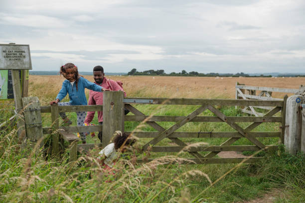 A wide angle front view of a little girl climbing over a fence as she enjoys a day out with her father and her little sister in the coastal town of Beadnell in the North East of England.