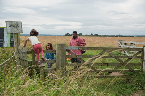 A wide angle view of a father and his tow daughters as they explore the beach and countryside in Beadnell in the North East of England. His youngest daughter is climbing over a fence into a field.