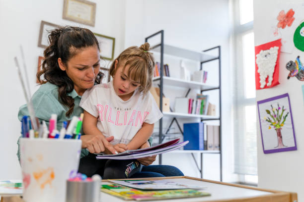 little girl with down syndrome reads a book with teacher - downs syndrome work bildbanksfoton och bilder