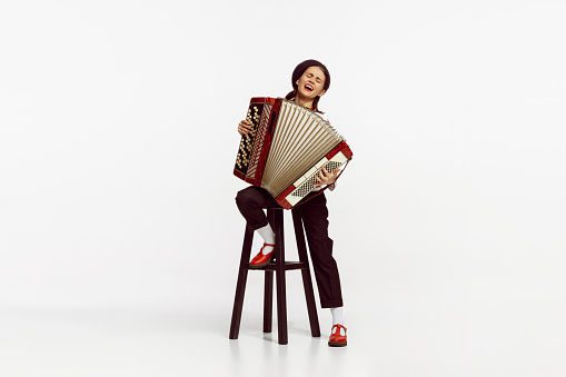 Portrait of talented beautiful woman playing accordion isolated over white studio background. Emotions. Concept of live music, performance, retro style, creativity, artistic lifestyle