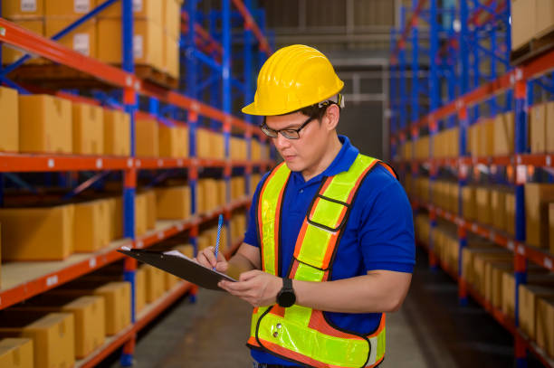 istock Young worker wearing helmet checking inventory and counting product on shelf in modern warehouse. 1422203597