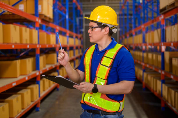 istock Young worker wearing helmet checking inventory and counting product on shelf in modern warehouse. 1422203655