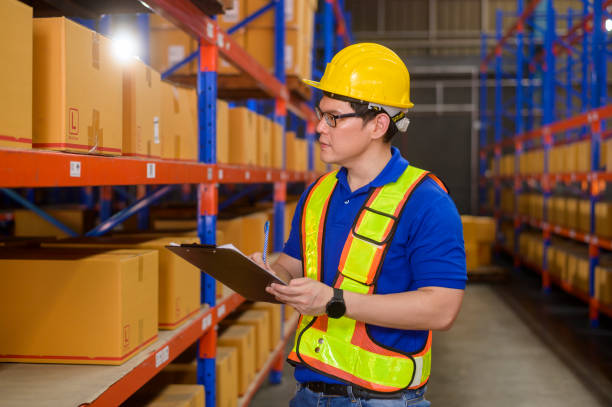 istock Young worker wearing helmet checking inventory and counting product on shelf in modern warehouse. 1422203683