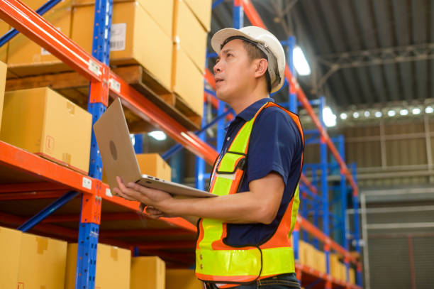 istock Young asian male worker wearing helmet using laptop in modern warehouse. 1422204245