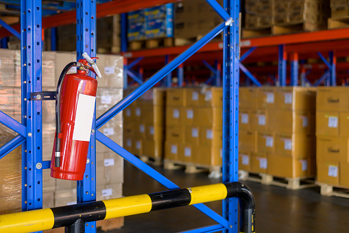 Fire extinguisher on shelf of cardboard boxes in modern warehouse.