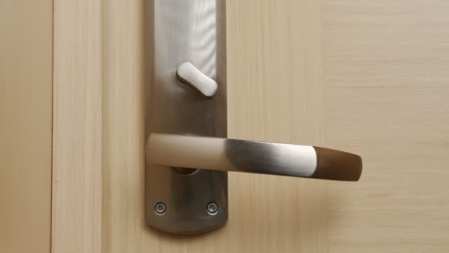 Woman closes wooden door turning safety knob on metal lock