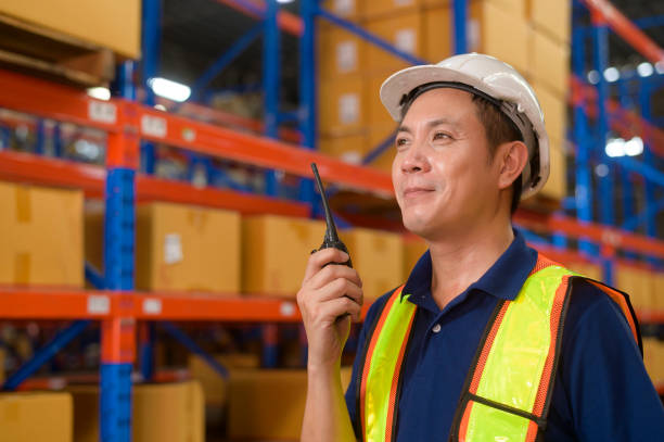istock Young asian male worker wearing helmet using talki walki in modern warehouse. 1422208023