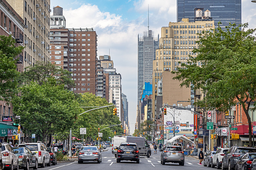 Manhattan, New York, NY, USA - July 12th 2022: View up the tree lined 8th Avenue with dense traffic and high rise buildings with wooden water tanks on the roofs