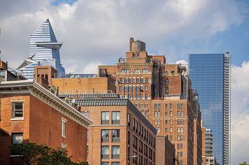 Manhattan, New York, NY, USA - July 12th 2022: Classic New York architecture with high rise brownstone buildings with a cedar wood water tank on the roof at 9th Avenue and modern skyscrapers at Hudson Yard behind
