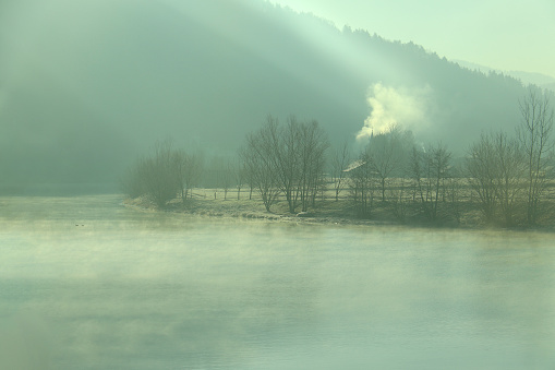 Cold morning scene on a lake shore with smoke coming up from a chimney.