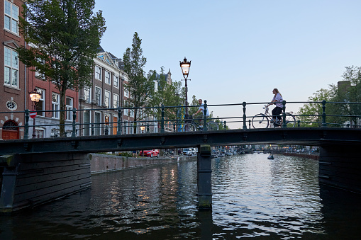 City canal bridge with people on bicycles at summer evening, Amsterdam, The Netherlands.