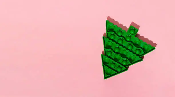 Photo of Anti stress pop it toy in form of green Christmas tree falling down on pink backdrop. Copy space.