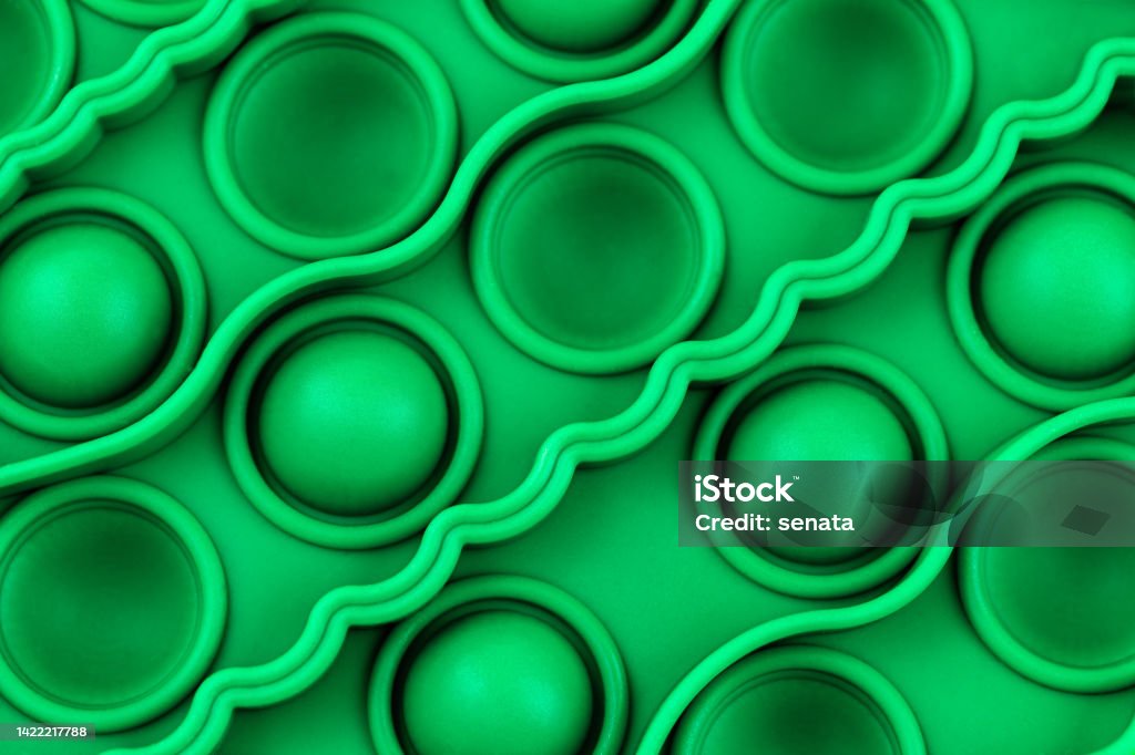 Relief surface of green silicon anti stress sensory pop it toy with with bumps and pits close up. Relief surface of green silicon anti stress sensory pop it toy with with bumps and pits close up. Popular calming toy for hyperactive kids. View from above. Push Pop Fidget Toy Stock Photo