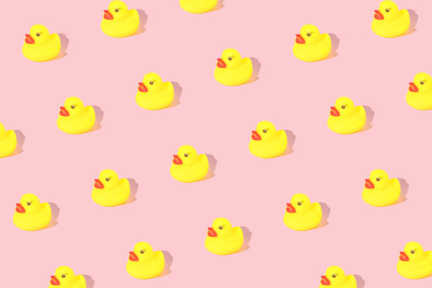 Creative pattern made with yellow rubber duck  on pastel pink background. Surreal bathing concept. Retro style aesthetic idea.