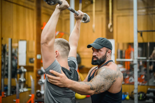 istock Man doing exercises in the gym with a man trainer athletic physique 1422224116