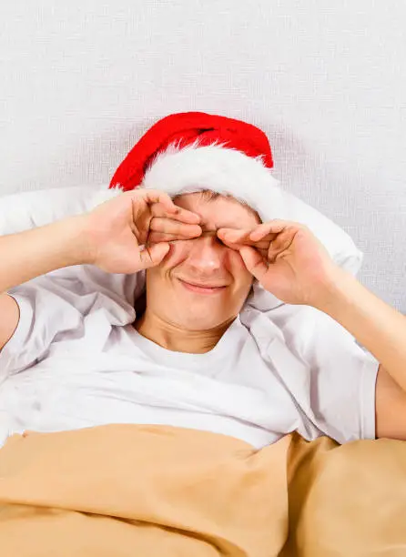 Tired Man in Santa Hat rub an Eyes in the Bed