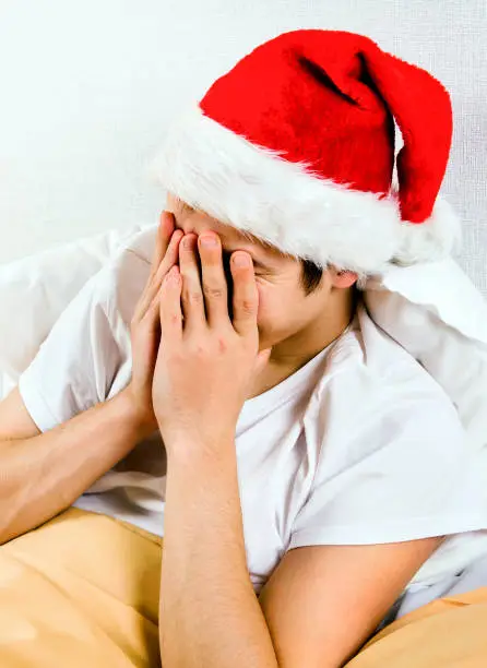 Sad Man in Santa Hat hide a Face in the Bed