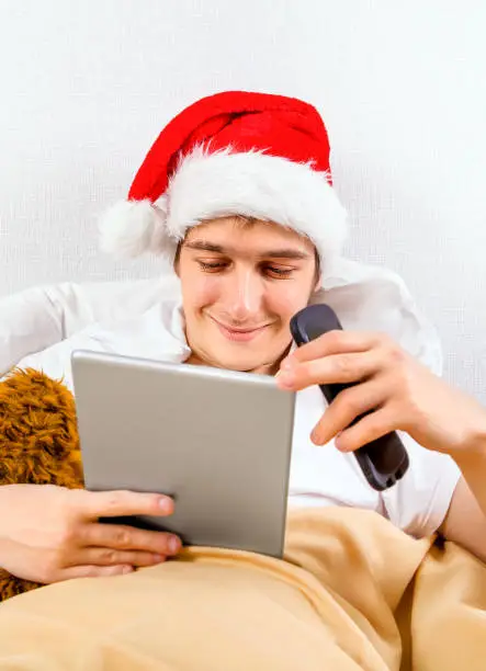 Man in Santa Hat with a Tablet and a Phone in the Bed