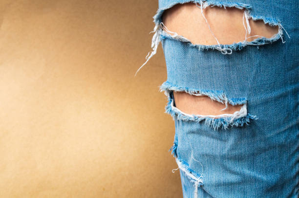 Leg in a torn jeans closeup Leg in a torn jeans closeup, tattered jeans on a light brown background with a place for your text hole in pants stock pictures, royalty-free photos & images