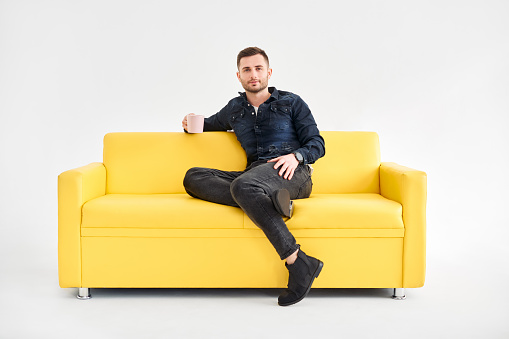 Relaxed man with coffee mug in hands sitting on comfort bright sofa looking to camera. good morning concept