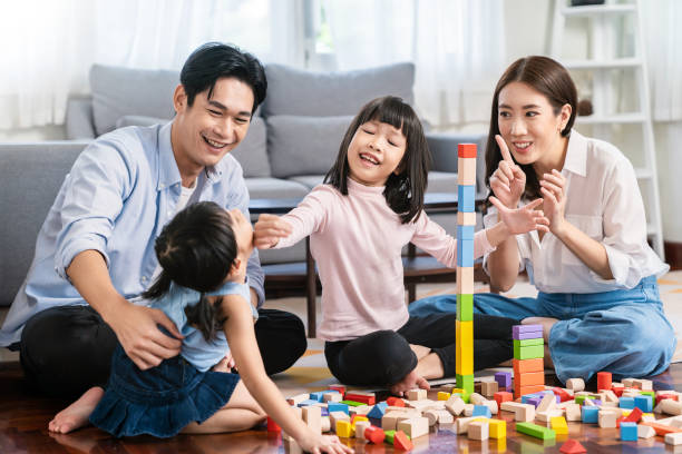 porträt eines asiatischen kleinen süßen mädchens, das bunte blöcke mit der geschwisterfamilie im wohnzimmer spielt. learning by playing education home school concept. muttereltern bringen ihrer tochter bei, blöcke zu spielen. - korea child baby asian culture stock-fotos und bilder