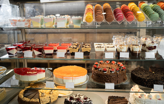 Many colorful delicious pastries and cakes in a glass showcase in a pastry shop close-up. Appetizing pastel sweet desserts on display with cream filling. Assorted pastry dough or pastry cake