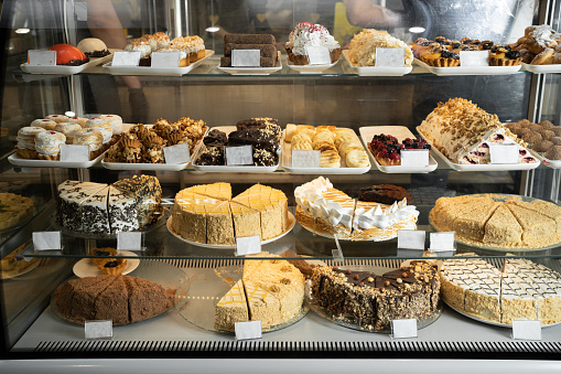 Pastry shop glass display with selection of cream or fruit cake, bakery shop with various flavors of cake