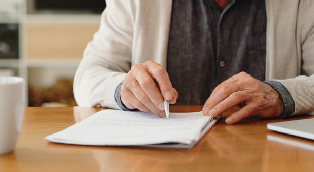 Hands of senior retirement woman writing a finance savings budget plan on paper or legal trust fund for after her funeral. Elderly person apply for pension or government financial support and help stock photo