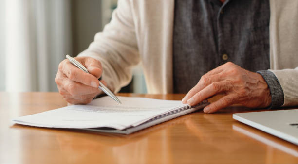 les mains d’un homme de pension lisent des documents de retraite sur la police, les options de placement et la couverture funéraire tout en planifiant les finances, les assurances et le budget à la maison. signature du testament, du document juridique  - document reading human hand caucasian photos et images de collection