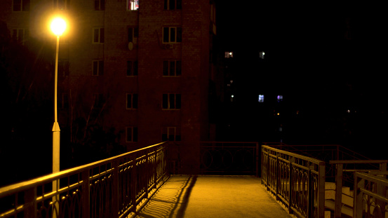 Lighted empty pedestrian bridge lit by the only street lamp. Empty pedestrian bridge over road with no people at nigh time with street light on.